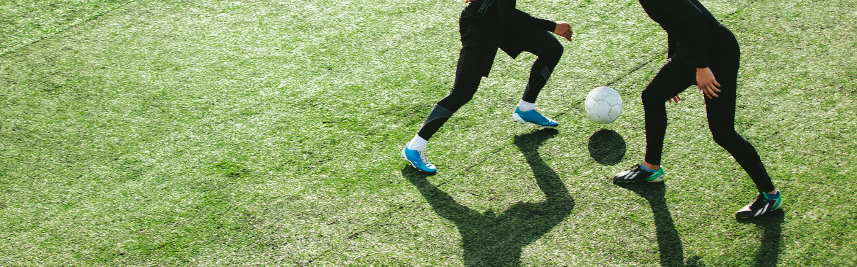Two people playing soccer on green field.