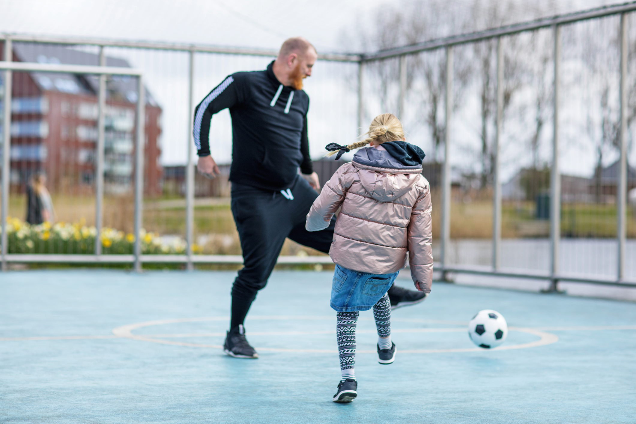 Adult and child playing soccer on court.