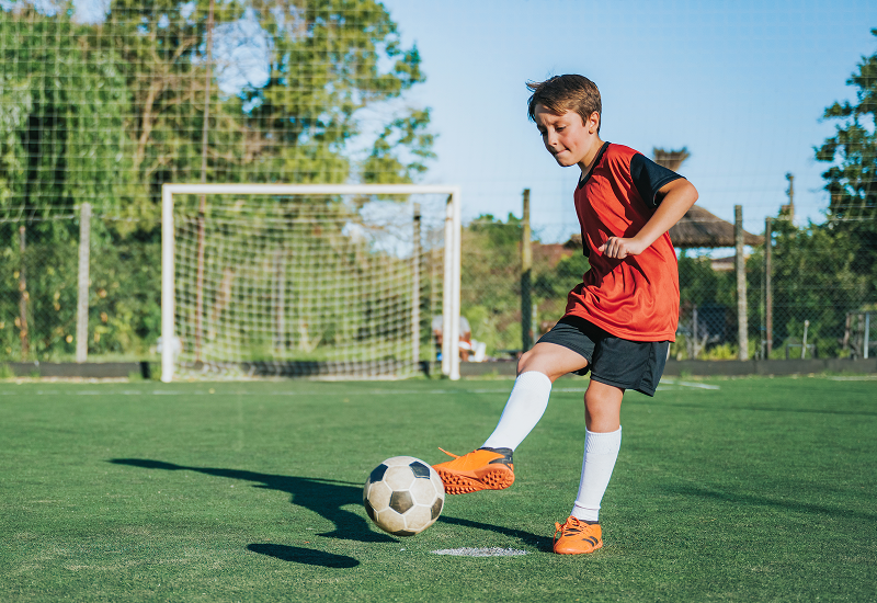 A young boy skillfully kicks a soccer ball on a sunny field, capturing the joy of playing outdoors.
