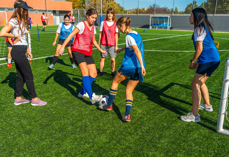 A group of young women actively playing soccer on a grassy field, showcasing teamwork and athleticism.