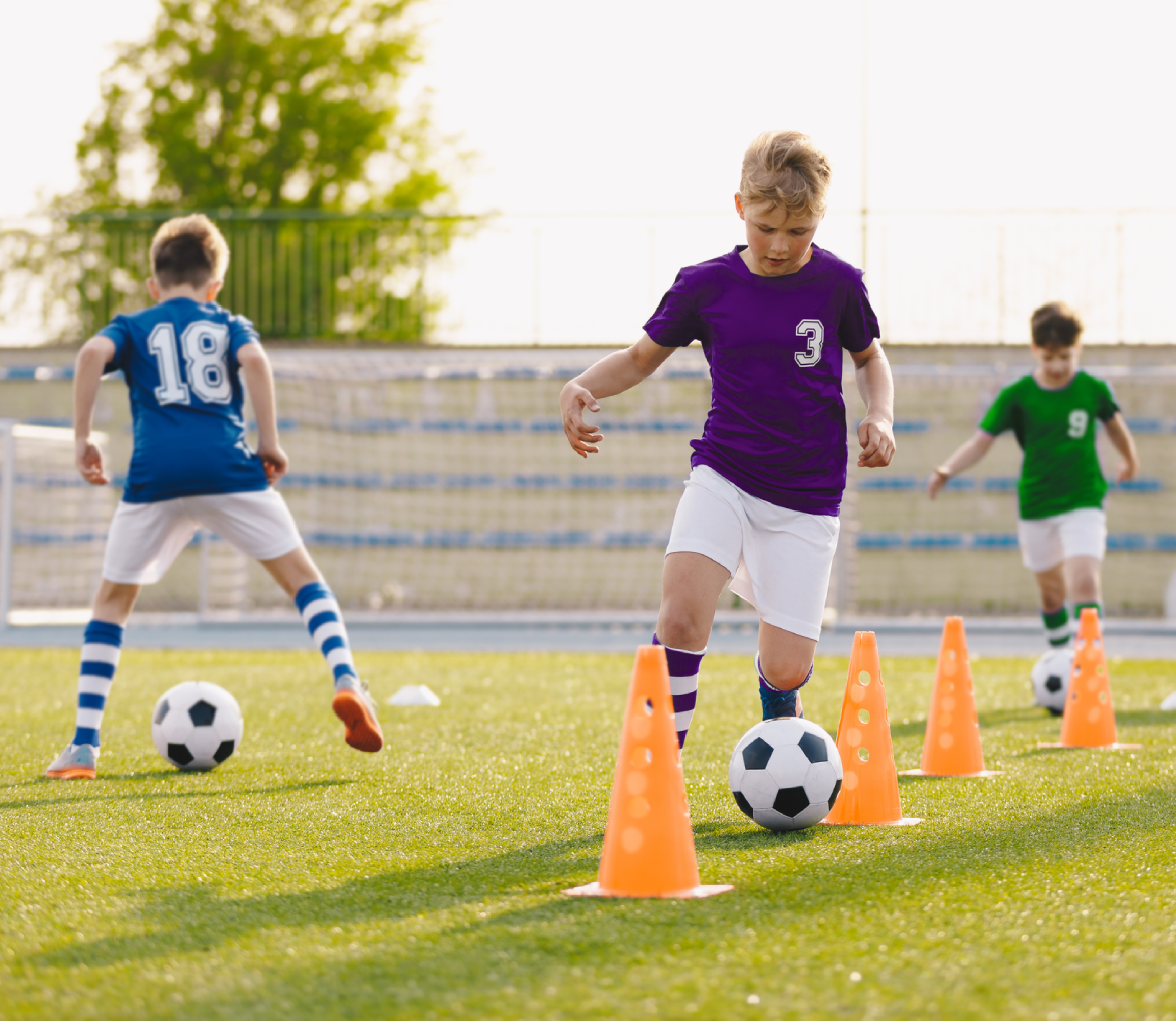 Kids practicing soccer with cones on field.