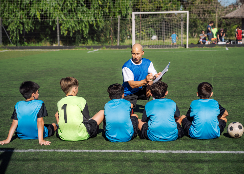 Soccer coach instructing young players on field.
